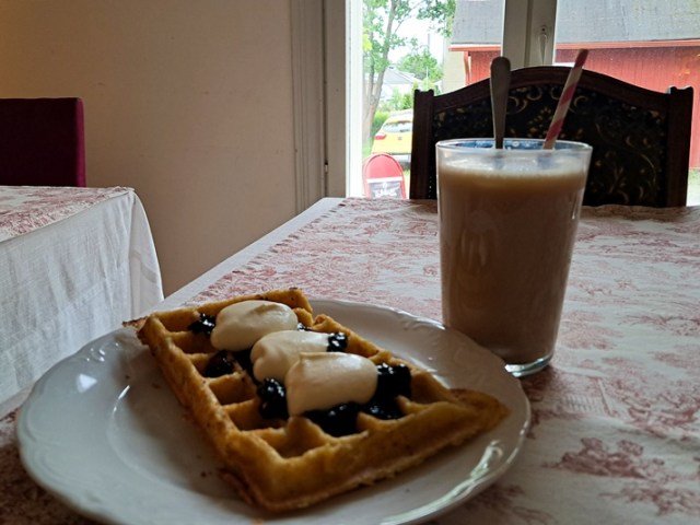 Kuvassa vohveli lautasella kermavaahvon ja hillon kanssa sekä jääkahvi