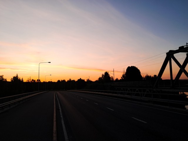 Aurinko nousee juuri, sillat, katuvalot ja metsä näkyvät tummina siluetteina.