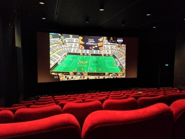 Kuva hämärästä elokuvasalista. Etualalla punaiset tuolit, taka-alalla valkokangas