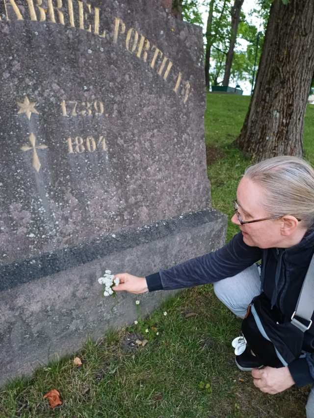 Ihminen ojentamassa kukkia haudalle.