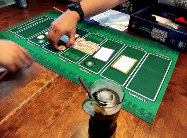 Vihreä pelilauta, asetetut arvaukset, panokset ja kaksi pelaavaa kättä. Etualalla on lasi juomalla