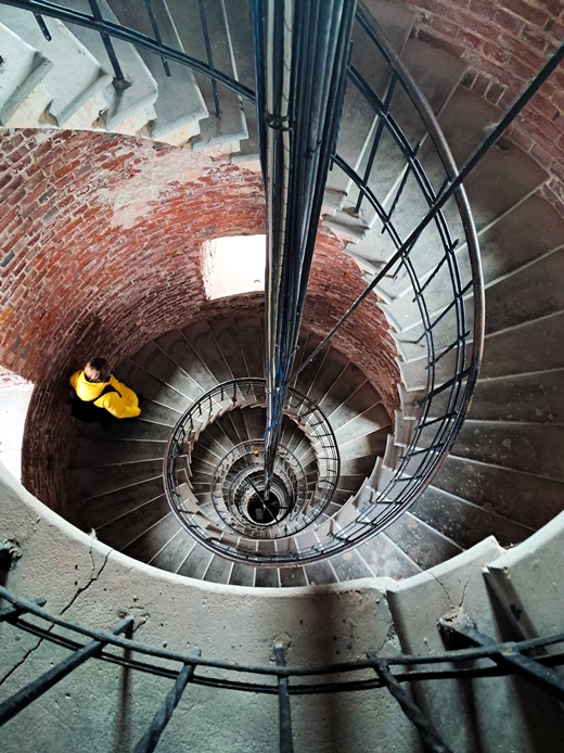 Majakann kierreportaat, keskeltä nousee kaapeleita. Portaissa kävelee keltaiseen takkiin pukeutunut henkilö.