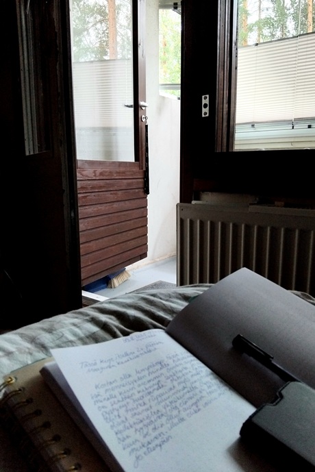 Avonainen parvekkeen ovi, etualalla vihko, jossa kirjoitusta.